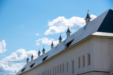 Siyah çatılı, beyaz, eski bir bina. Altın bayraklı küçük kulelerle süslenmiş..