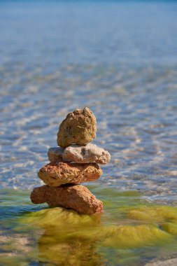 Saf deniz suyunun arka planına karşı bir piramide istiflenmiş desenli taşlar. Metin ve tasarım için boşluk kopyala.