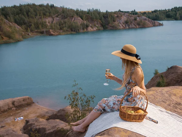 Hasır şapkalı güzel bir kız, elinde piknik sepeti ve elinde bir bardak şampanyayla nehrin yukarısındaki yüksek bir kıyıda.