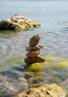 Saf deniz suyunun arka planına karşı bir piramide istiflenmiş desenli taşlar. Metin ve tasarım için boşluk kopyala.
