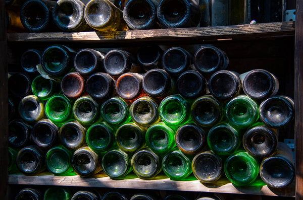 Dusty wine bottles are stacked on racks, and a wooden crate of juicy fruit stands next to them.