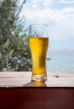 Buğulanmış bir bardak bira, deniz manzarasının arka planında duruyor..