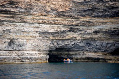 Kırım, Tarkhankut Burnu, Ağustos 2020. Motoru olan şişme bir teknede turistler büyük bir kayanın içinde mağaraya yüzerler..
