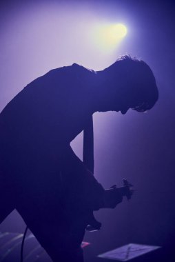 Hafif bulanık bir siluet. Genç bir adam, sisli bir ışıkta gitar çalıyor..