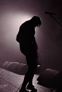 Monokrom fotoğrafçılık. Hafif bulanık bir siluet dumandaki gitarlı genç bir adam, bir kontür ışıkla aydınlatılmış..