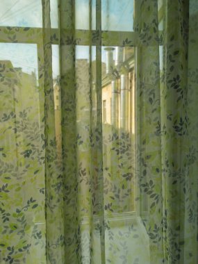 Açık renkli perdeyle kaplı bir oda penceresi. Güneş ışınları tülleri delip geçiyor..