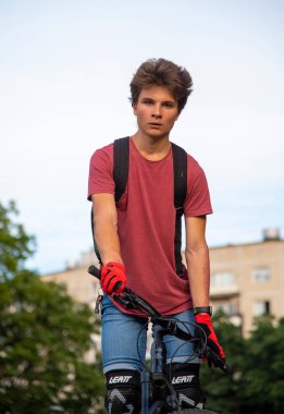 Rusya, Moskova, Eylül 2020. Kırmızı tişörtlü genç bir adam bisikletle gökyüzüne karşı poz veriyor..