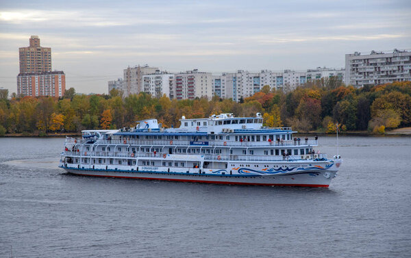 Russia, Moscow, October 2020. A cruise ship sails along the Moscow river against the background of autumn trees and high-rise residential buildings.
