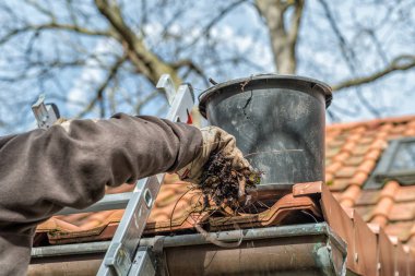 Man on a ladder cleaning house gutters clipart