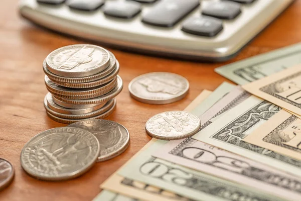 Montón de monedas con billetes de dólar y una calculadora —  Fotos de Stock