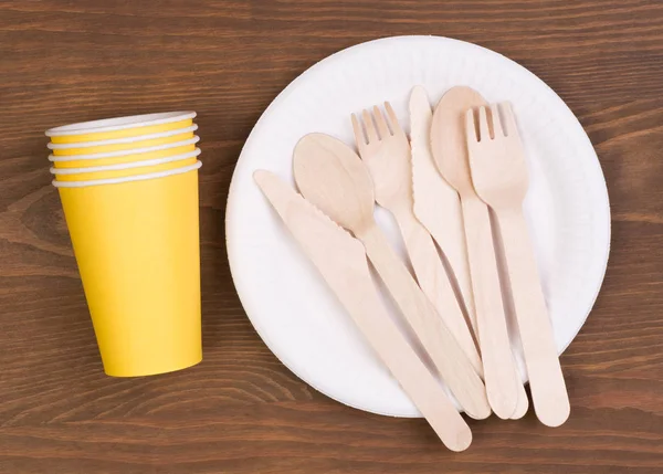 Disposable paper plates and cups and wooden cutlery on wooden table