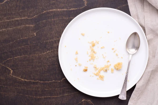 stock image Empty white plate with crumbs on dark wooden background, top view