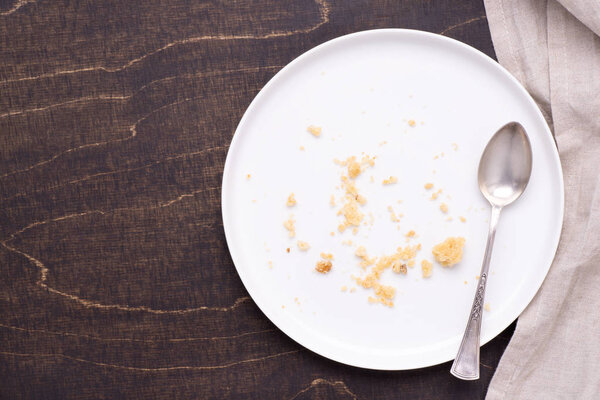 Empty white plate with crumbs on dark wooden background, top view
