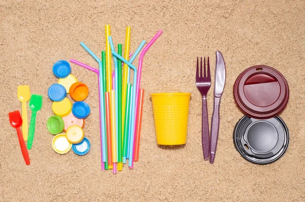 Disposable single use plastic objects such as bottles, cups, forks, spoons and drinking straws that cause pollution of the environment, especially oceans. Top view on sand