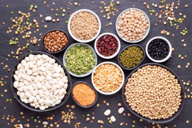 Legumes, mercimek, nohut ve fasulye çeşitleri çeşitli kaseler üzerinde siyah taş arka plan, üst görünüm