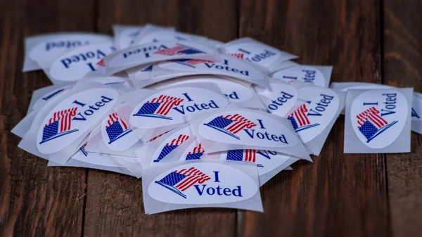 コロラド州の予備選挙のときに投票所の上に木製のテーブルの上に座っている赤白と青の有権者のステッカーの山投票を投票した後に有権者に提供される — ストック写真