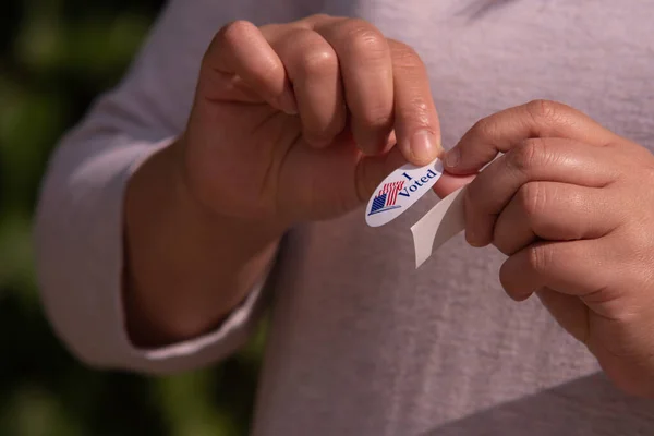 赤い白と青の楕円形を剥がす外に立つアメリカ人女性私は選挙で投票した後 シャツに置くために彼女の指に保持を投票ステッカー — ストック写真