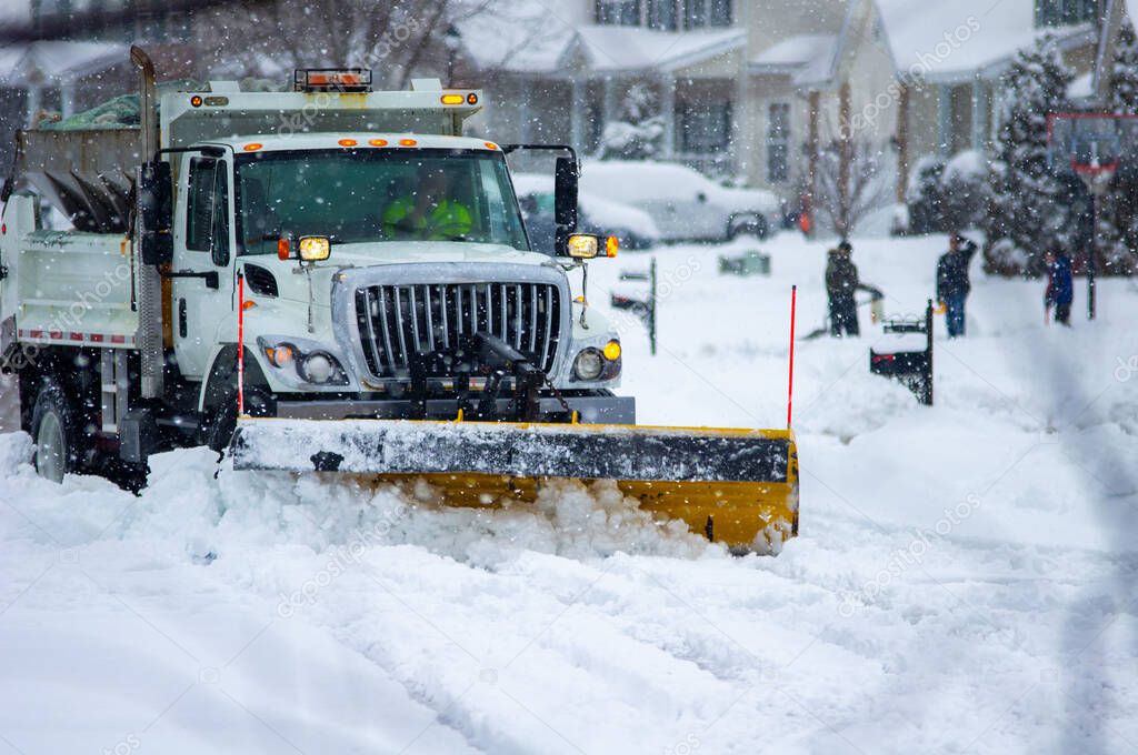 Front right view of city services snowplow truck clearing roadways of snow after winter storm covered streets in urban area