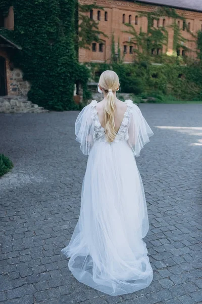 若いつるで覆われた古代の建物の前で美しいウェディング ドレス花嫁の背面図 — ストック写真