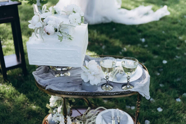 table with wedding cake and glasses of champagne on green grass