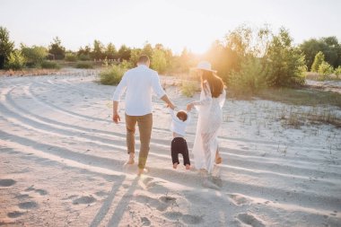 arkadan görünüşü elele ve bebek çocuk ile sahilde yürüyüş mutlu aile
