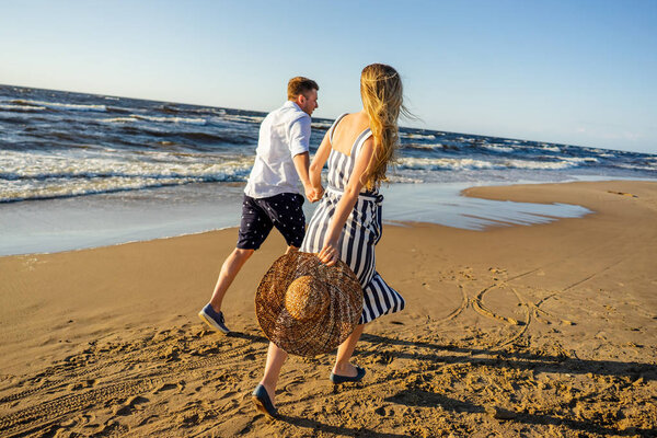 partial view of young couple in love holding hands and running on sandy beach in Riga, Latvia
