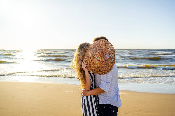 partial view of couple in love hiding behind straw hat on sandy beach in Riga, Latvia