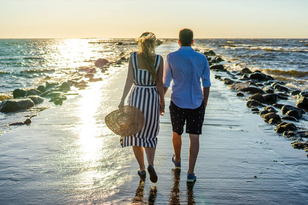 back view of couple in love walking on seashore during sunset in Riga, Latvia