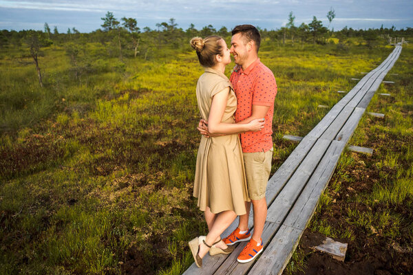 smiling couple in love hugging each other on wooden bridge with green plants on background