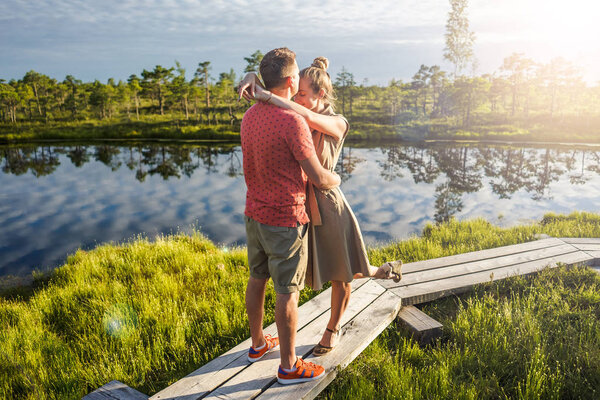 couple in love hugging each other on wooden bridge with green trees and river on background