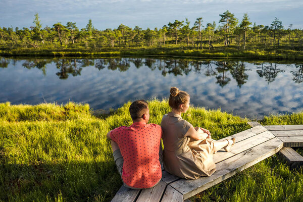 couple in love sitting on wooden bridge with river and green trees on background