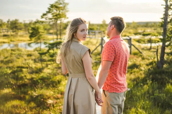 恋の背景に緑の植物と木の橋の上で手を繋いでいるカップルの背面図 — ストック写真