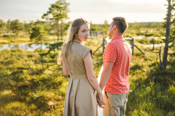 back view of couple in love holding hands on wooden bridge with green plants on background