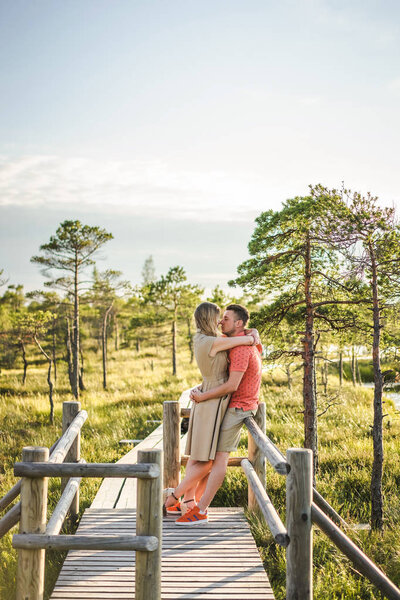 side view of affectionate couple hugging on wooden bridge with green plants and blue sky on background