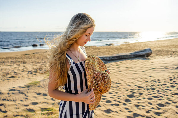 side view of attractive young woman with straw hat on sandy beach in Riga, Latvia