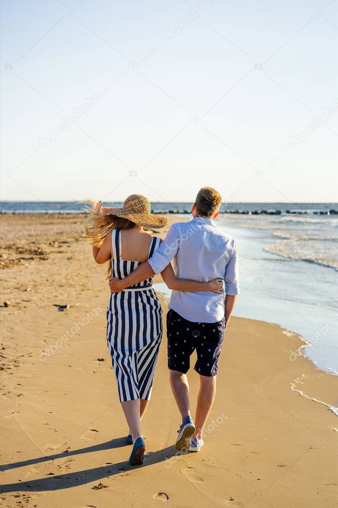 rear view of affectionate couple walking on sandy beach on summer day