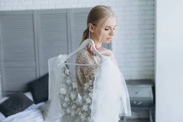 Belle jeune mariée tenant robe de mariée blanche sur cintre — Photo de stock