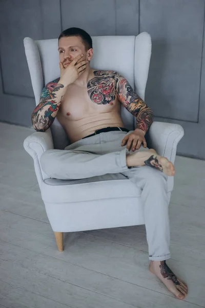 Hemdloser junger Mann mit Tätowierungen sitzt im Sessel — Stockfoto
