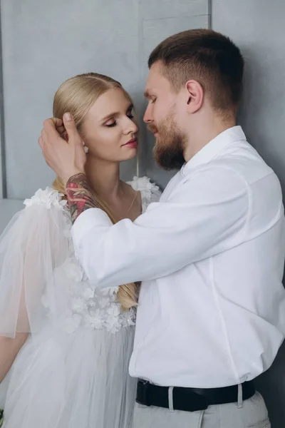 Belle jeune mariée et marié baisers devant le mur gris — Photo de stock