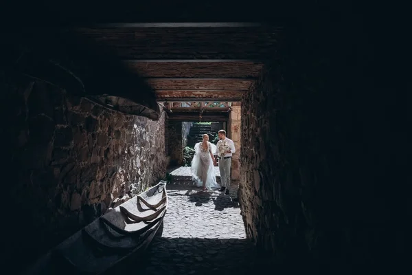 Noiva e noivo caminhando em portão do castelo antigo — Fotografia de Stock