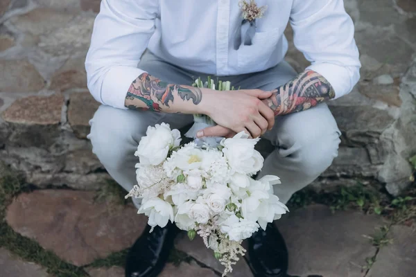 Cropped shot of groom with bridal bouquet sitting on stone stairs — Stock Photo