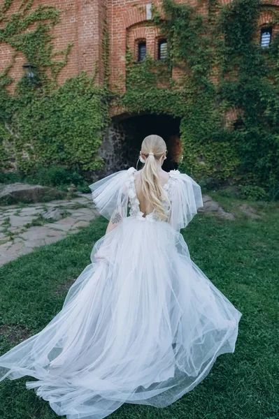 Vista trasera de la novia joven en hermoso vestido de novia en frente del edificio antiguo cubierto de vid - foto de stock