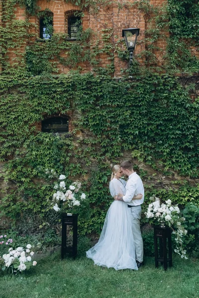 Braut und Bräutigam umarmen sich vor einem mit Weinreben und grünen Blättern bedeckten Gebäude — Stockfoto