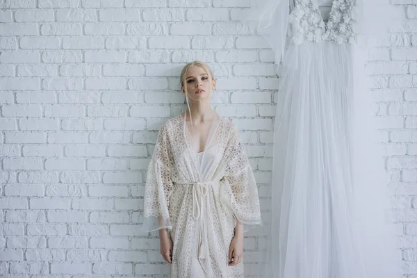 Jeune femme en négligee élégant devant un mur de briques blanches — Photo de stock