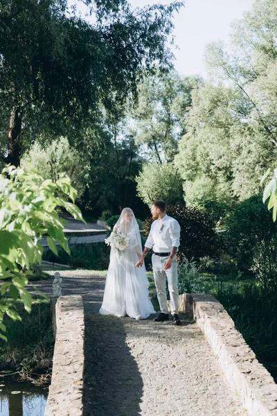 Braut und Bräutigam spazieren gemeinsam durch grünen Park — Stockfoto