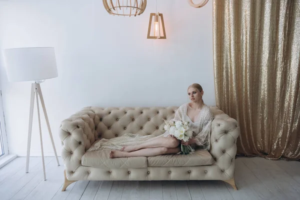 Sensual young woman sitting on couch with bouquet — Stock Photo