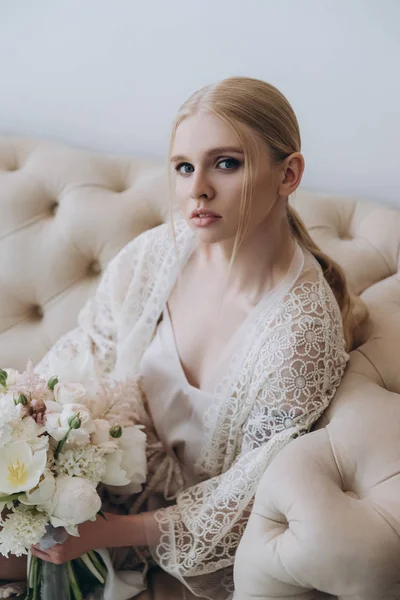 Attrayant jeune femme assise sur le canapé avec bouquet regardant la caméra — Photo de stock