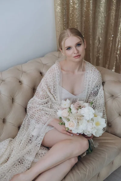 Attrayant jeune femme assise sur le canapé avec bouquet — Photo de stock