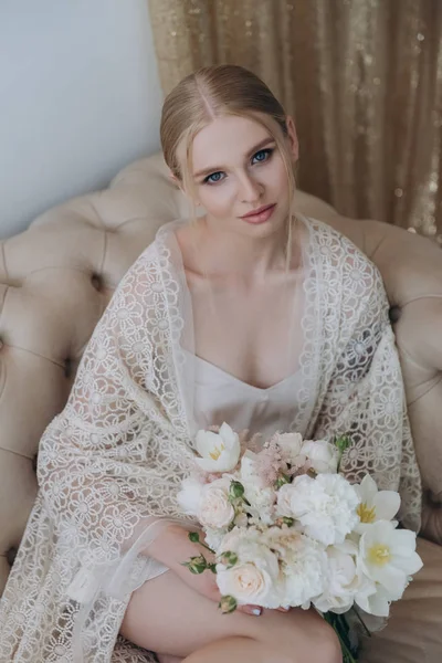 Belle jeune femme assise sur le canapé avec bouquet — Photo de stock