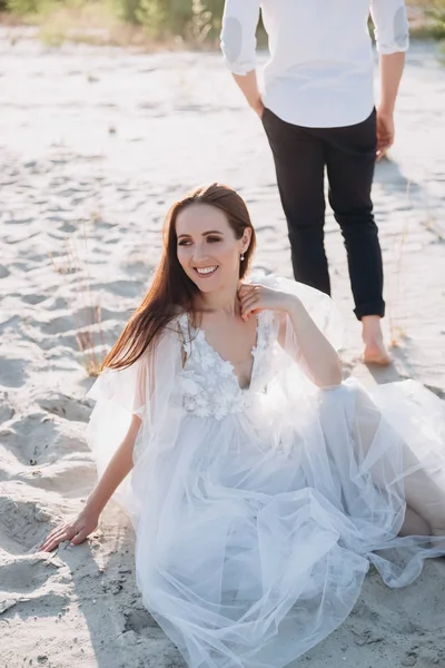 Jolie femme assise sur la plage, petit ami marchant derrière — Photo de stock